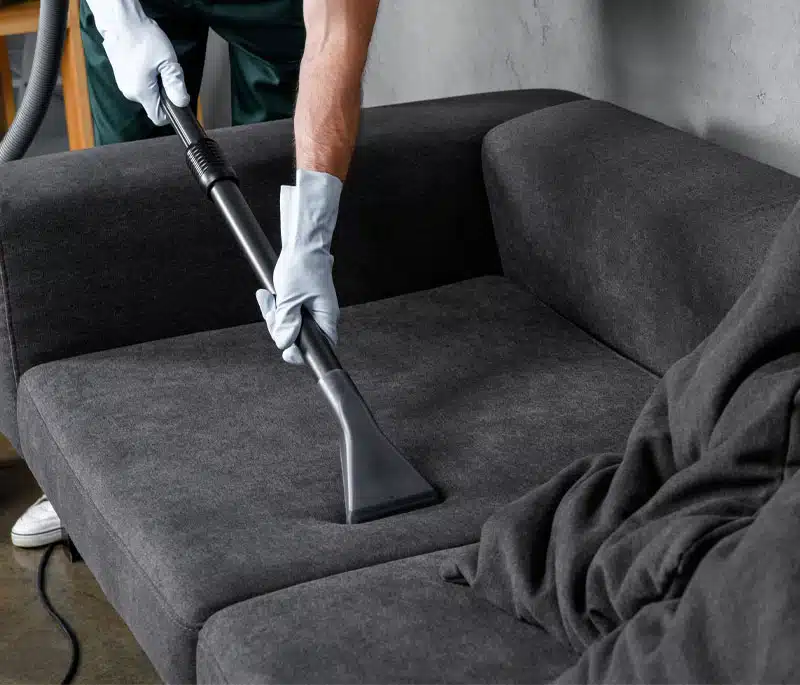 Upholstery cleaner leaning over dark grey couch they're cleaning