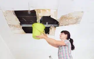 Woman holding bucket to collapsed ceiling water damage